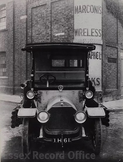 An old-fashioned car on a road outside a building with 'Marconi's Wireless Telegraph Works' painted on the corner.