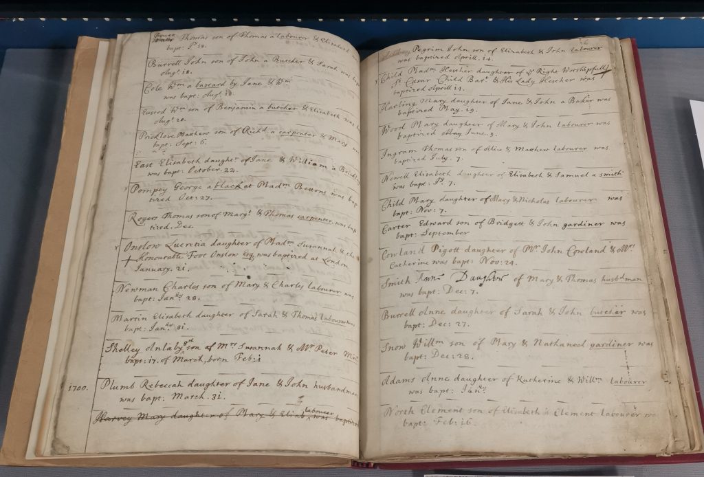 Photograph of an open parish register on display in a case in the Searchroom at the record office. The entries are all handwritten, and the relevant entry reads: "George Pompey, a black at Mdm Bettons, was baptised Oct 27".