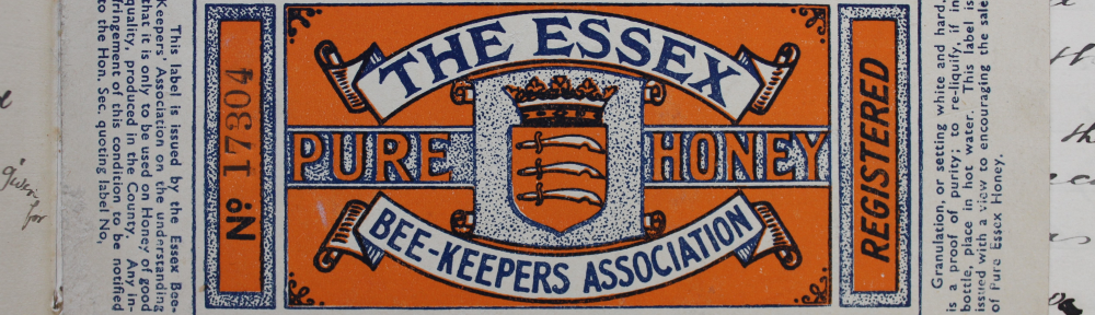 A thin cardboard label designed to wrap around a glass honey jar. Heraldic design with The Essex Beekeepers' Association" and "Pure Honey" written in banners around the Essex county coat of arms