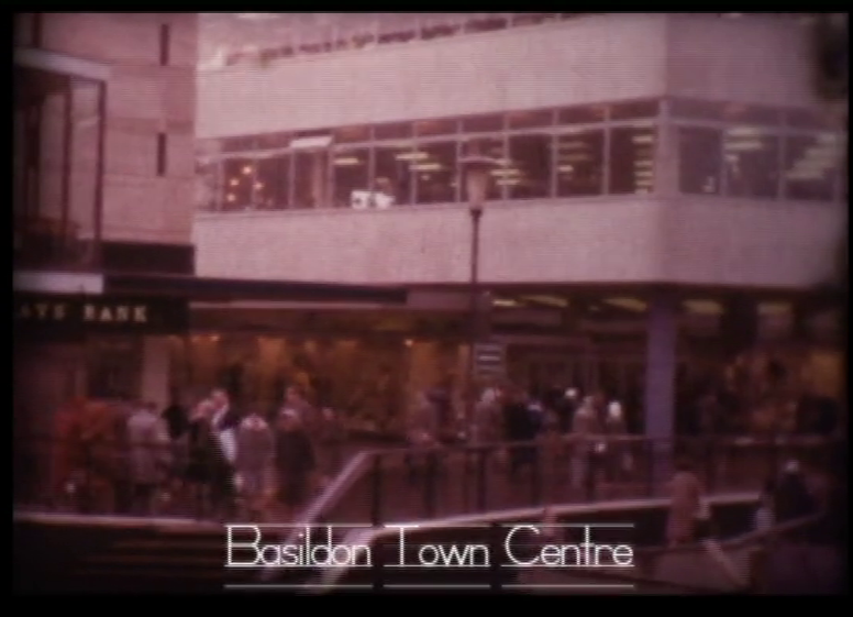 Still from a cine-film with white title 'Basildon Town Centre'. The image behind shows a multi-storey white building in the background with stairs in the foreground.