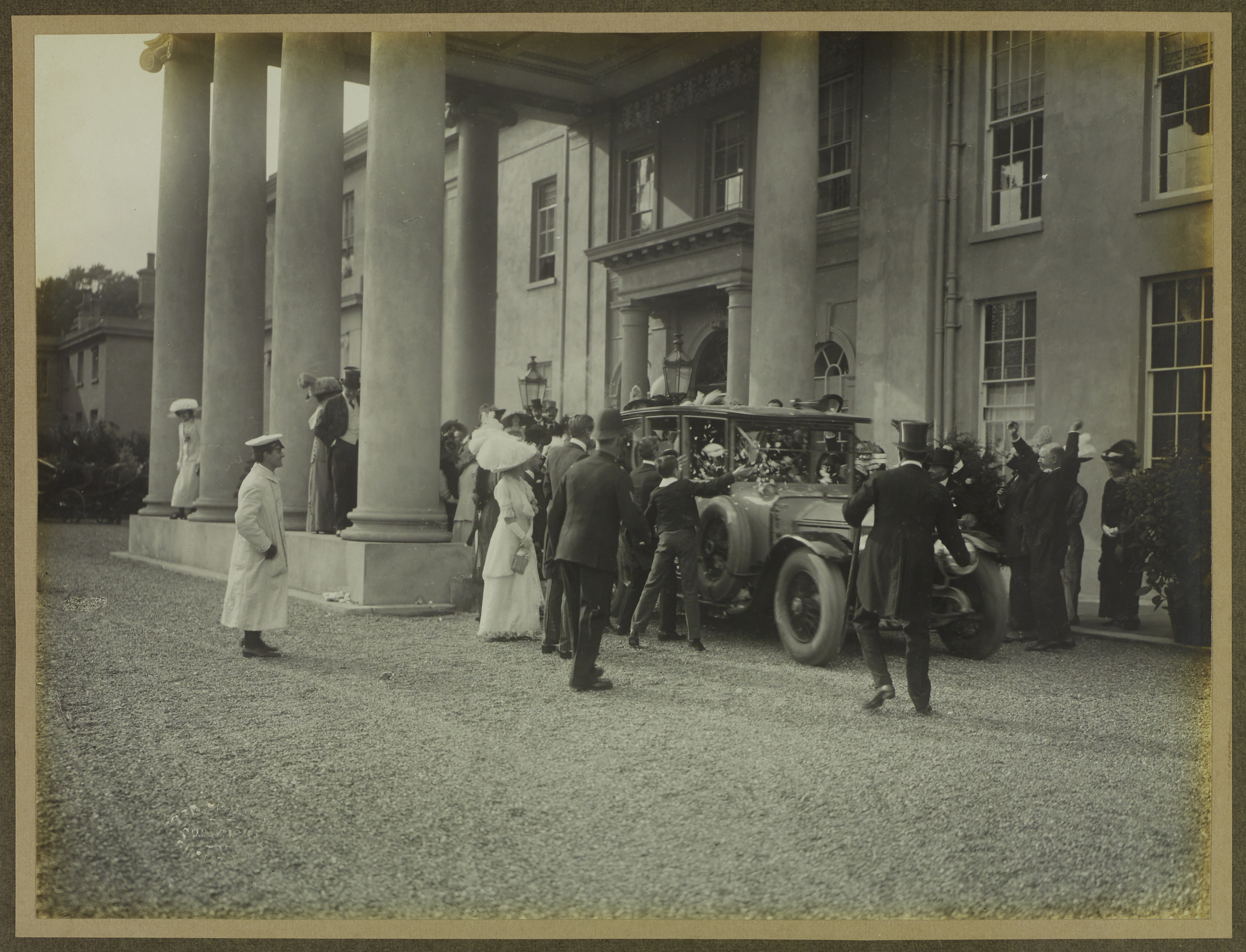 Black and white photograph of the bride and groom leaving by car surrounded by wedding party throwing confetti